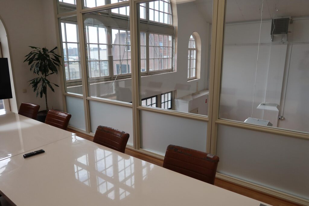 Vergaderruimte met leren stoelen, witte tafel en groot raam met uitzicht op het Gedempt Hamerkanaal.